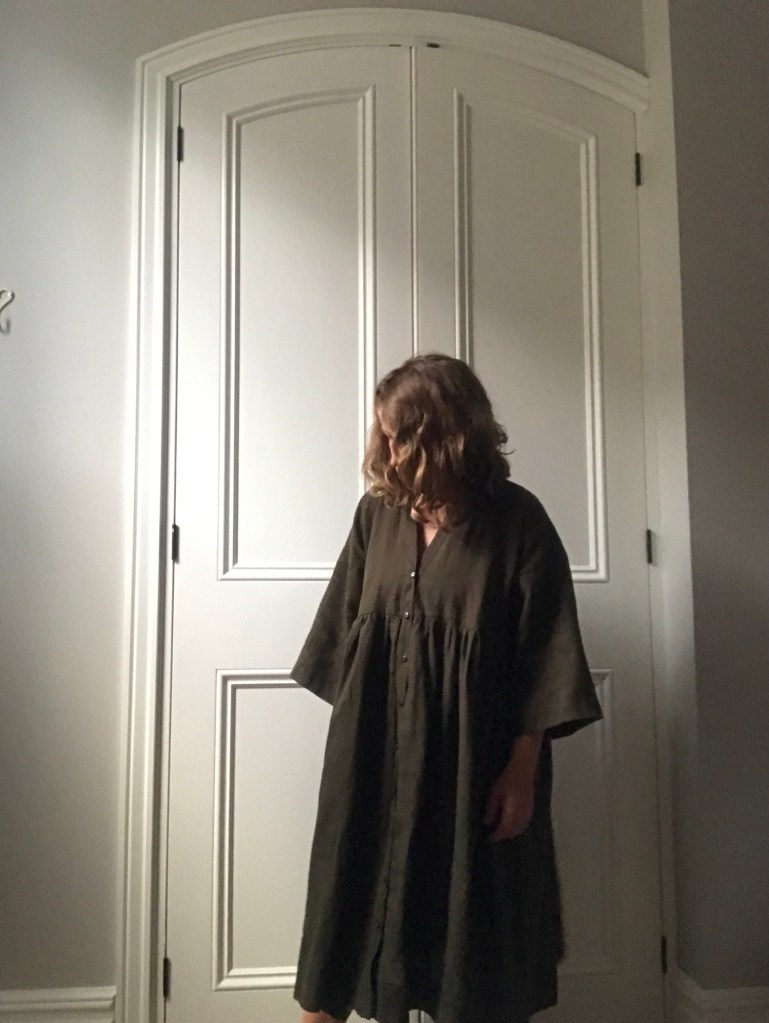 olive green linen ZW Zero Waste Gather Dress by Birgitta Helmersson worn in front of arched panel doors